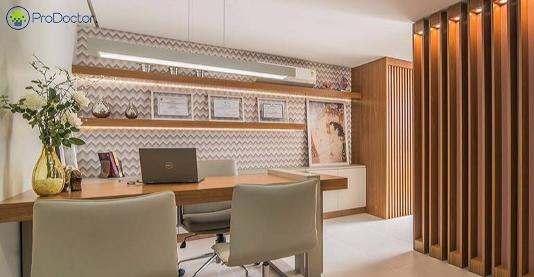 Consultório médico moderno com mesa de madeira, poltronas claras e painel ripado.